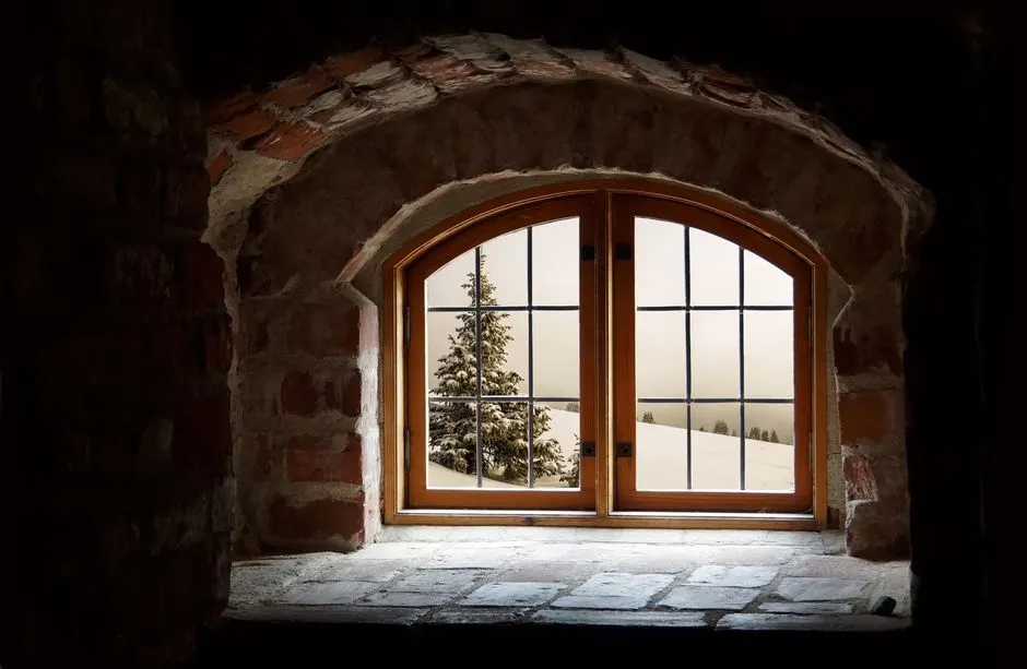 A rustic arched window opening to a snowy landscape, framed by stone walls and wooden accents.