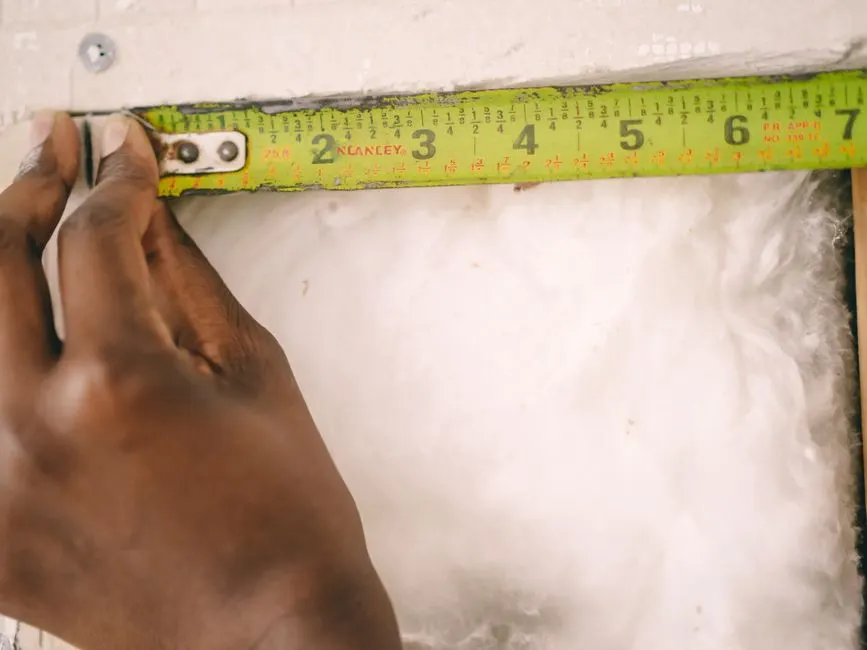 Close-up of a hand measuring insulation with a yellow tape measure.